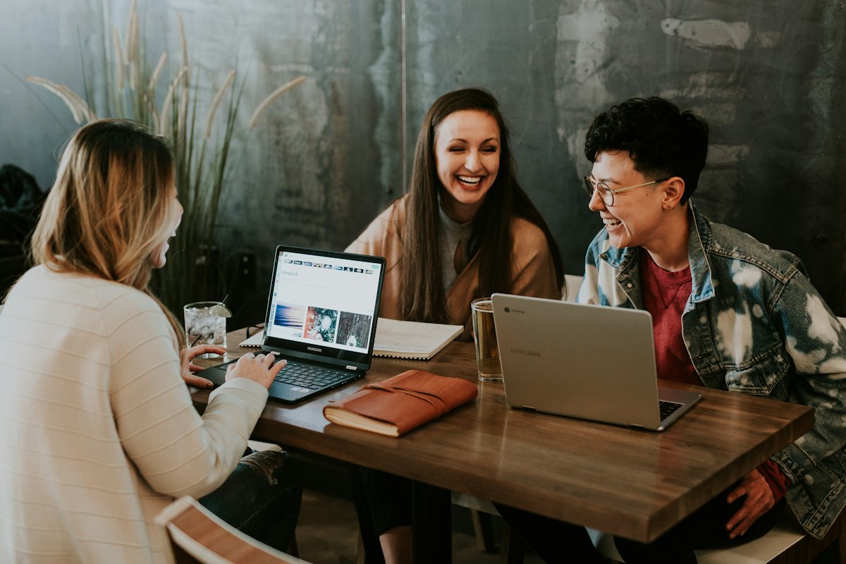 Real photograph of digital professionals collaborating around a table with laptops and project notebooks