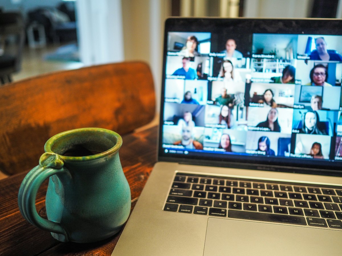 Real photo of a laptop display during an active multi-participant video conference call with coffee mug on desk